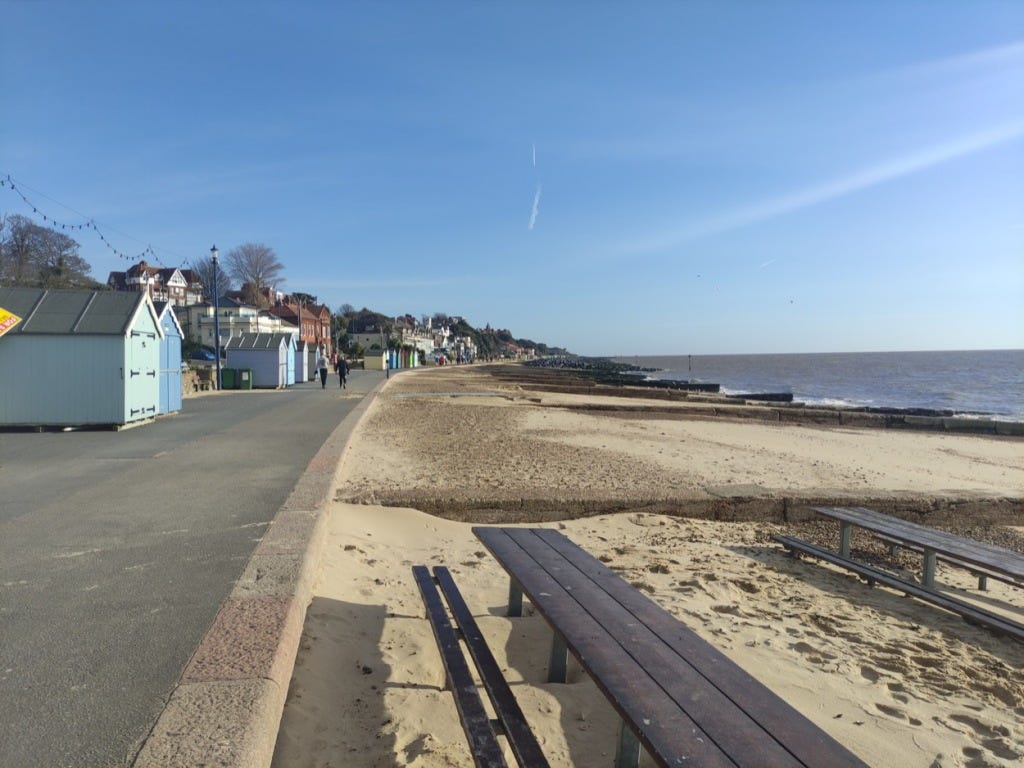 View North along the promenade, with beach huts on the left and sandy beaches on the right.