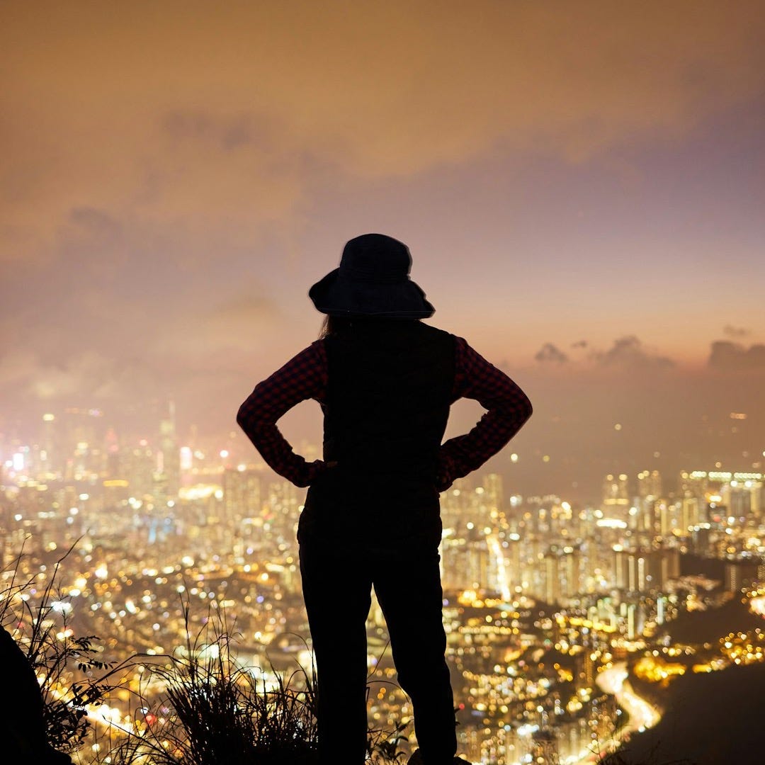 a person standing on a ledge overlooking a city at night a person standing on a ledge overlooking a city at night