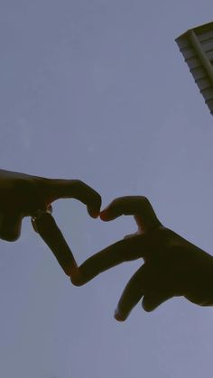 This may contain: two hands making a heart shape with their fingers in the air against a blue sky