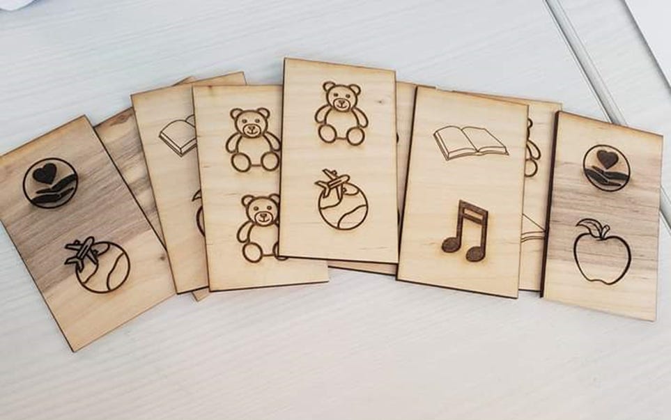 A pile of rectangular wooden tiles with symbols like teddy bears, apples, and globes fanned out on a table.