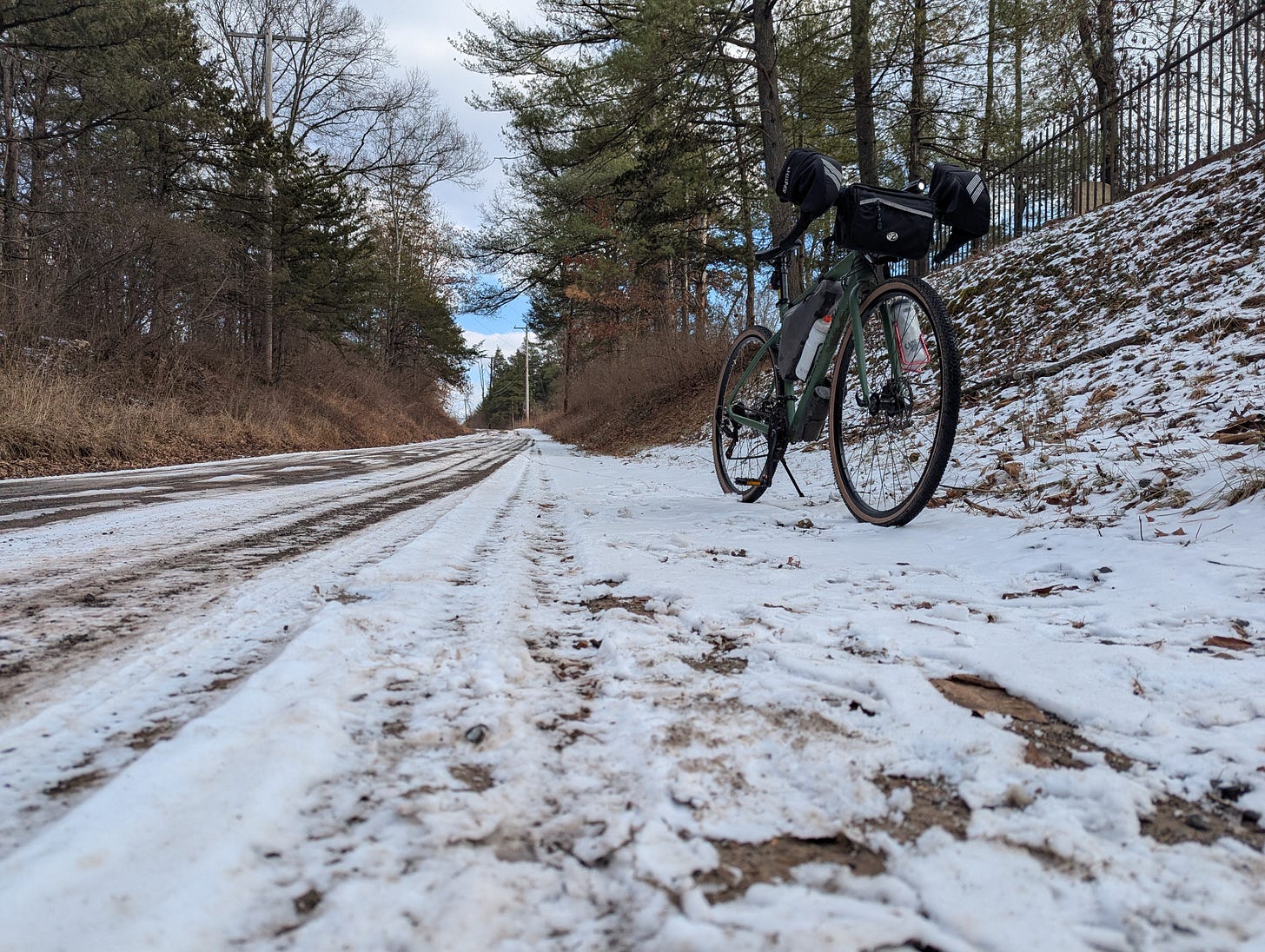 Photo looking up a hilly, snow-covered road. A bicycle stands parked on the side, facing the camera.