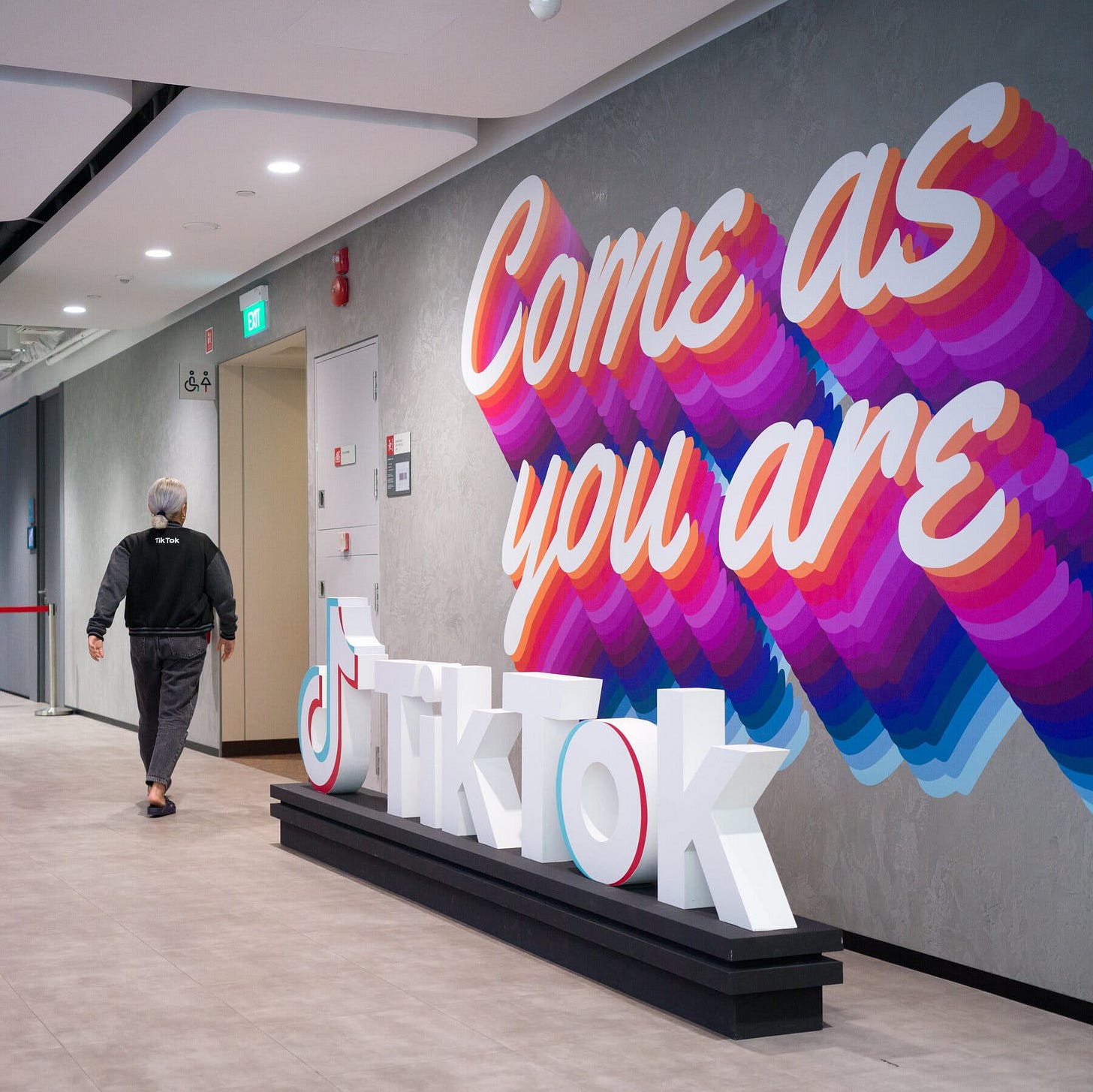 A person walking past a large mural that reads “Come as you are” and a sculpture of the TikTok logo.