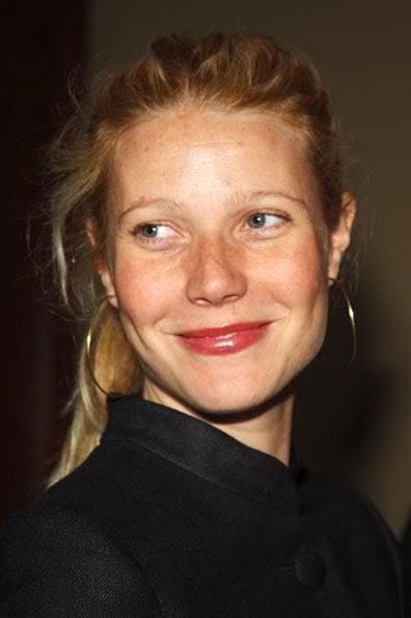 This may contain: a woman with blonde hair and blue eyes smiles at the camera while wearing large gold hoop earrings
