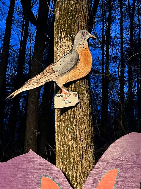 First image is a picture of an upright painted bat with pink ears hanging on a tree, second image is the entry way to the Batland Exhibit + Save the Woods party, next is a painted sign on fabric that reads KEEP ASHEVILLE GREEN, fourth is an image of the Batland Exhibit sign with Spencer Beals, my daughter, and me, fifth is a close up of the Batland Exhibit sign which is a map of the woods showing where the bats are placed- sixth is an image of a party goer with large homemade see- through bat wings posing in front of the sign, sevent is a home made painted sign that reads 'Chancellor to Helene "Hold My Beer! Watch Me Take All the Trees!" eight is an image of Spencer's painting titled "Eyes of Appalachia" and finally we have a hand made carrier pigion on a tree as part of the exhibit.