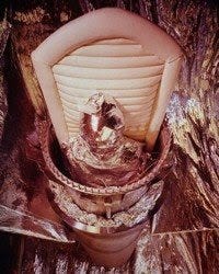 A man seemingly wrapped in tinfoil and strapped into a cynlinder
