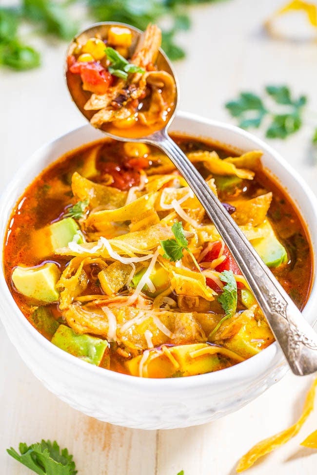 A bowl of homemade chicken tortilla soup, with a spoon resting on the lip. 