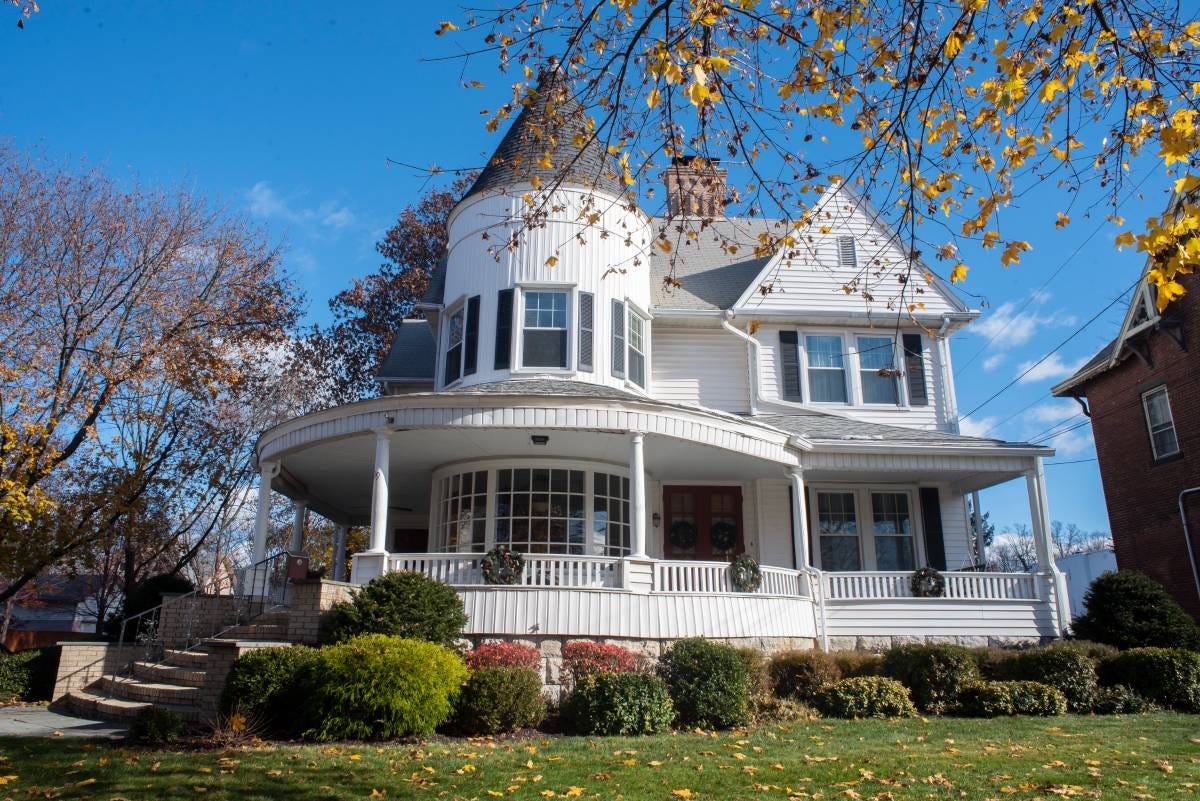 A white victorian home with round turret ad round broad front porch surrounded by a grassy lawn.