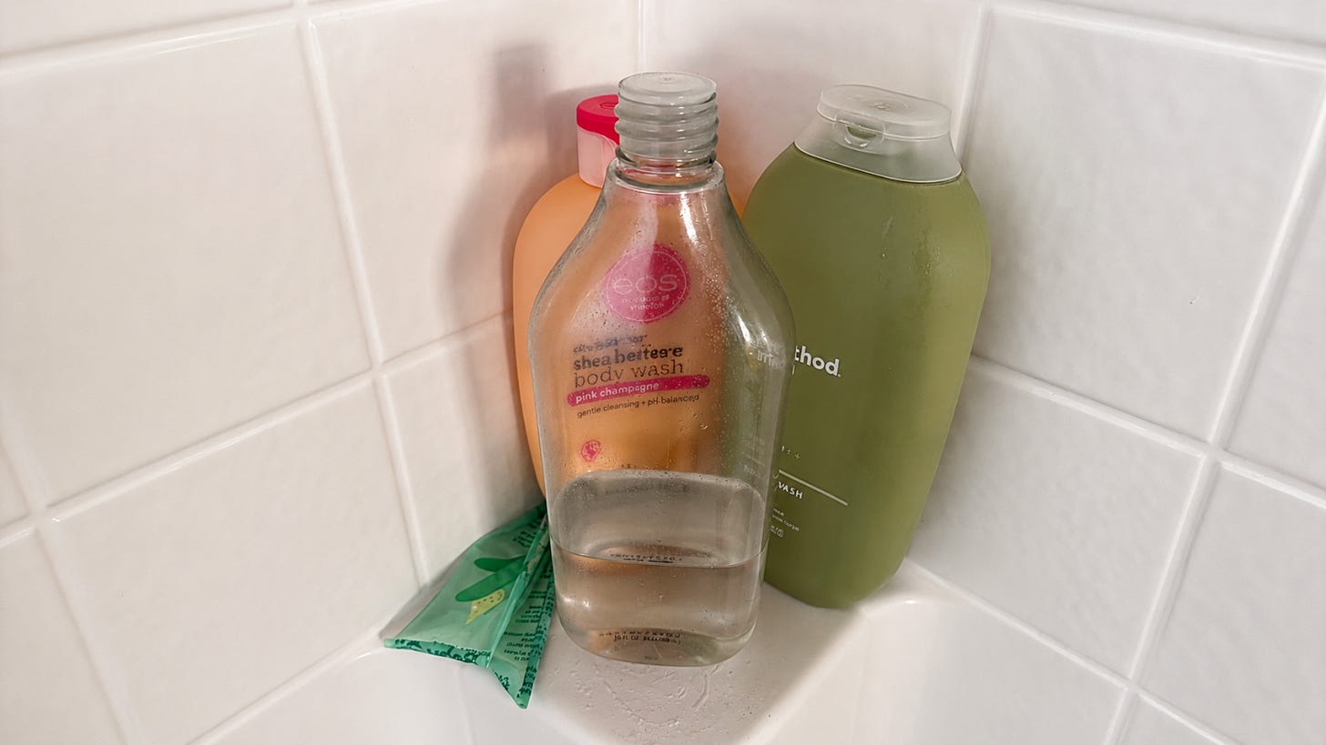 A clear baby oil bottle with its labels removed sits in a shower, illustrating how the bottle's contents remain visible even after the labels are gone—a visual metaphor for identity becoming clearer when false labels are stripped away.