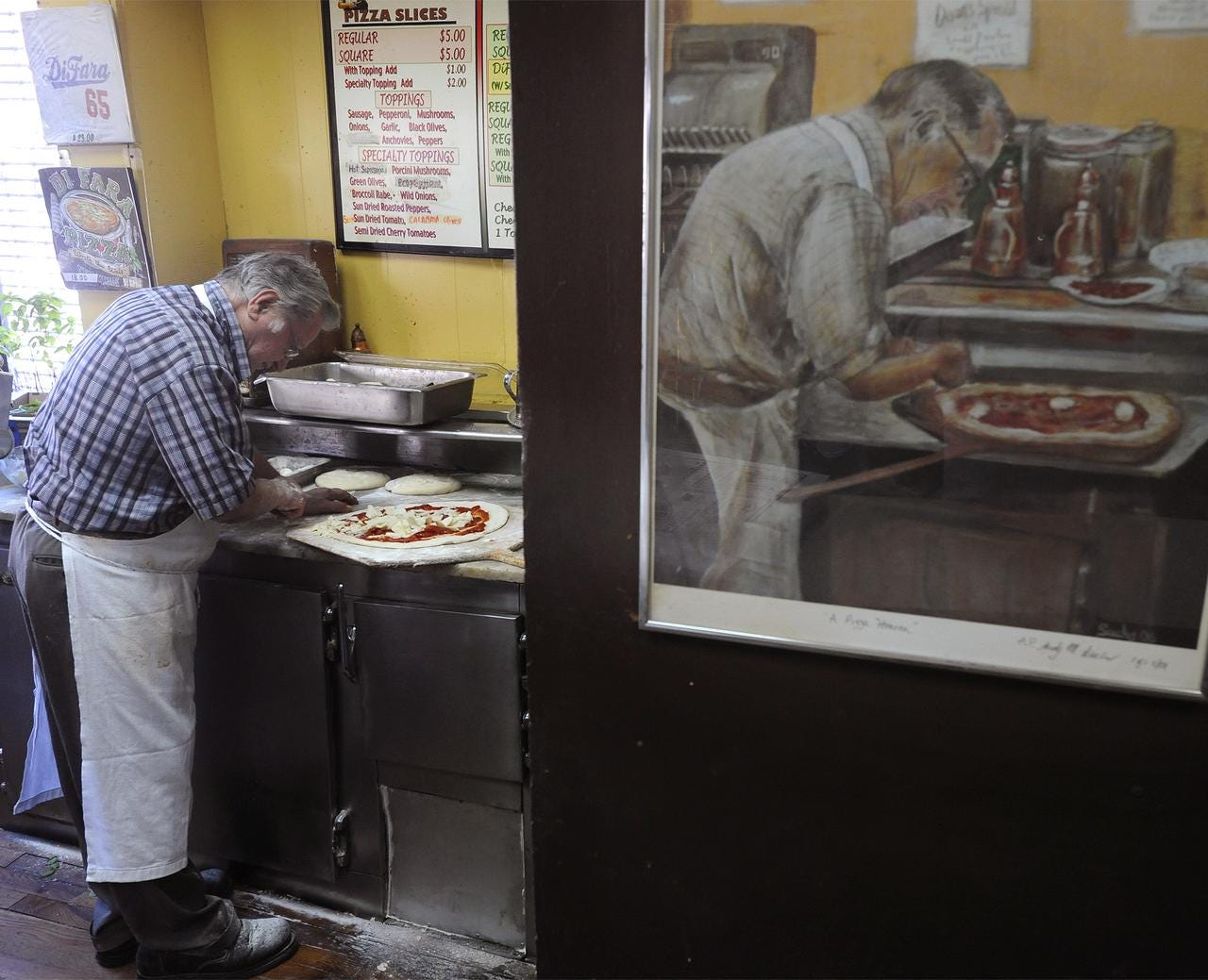 A painting of Dominick DeMarco, owner and cofounder of DiFara Pizzeria, hangs on the Midwood pizzeria's wall as DeMarco himself makes a pie.
