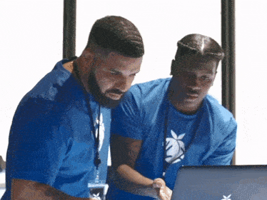 two men in blue shirts are looking at a laptop computer two men in blue shirts are looking at a laptop computer