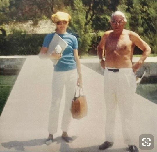 This may contain: an older man and young woman standing on a dock with their hands in their pockets