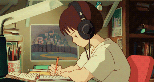 This may contain: a person sitting at a desk with headphones on and writing in a note pad