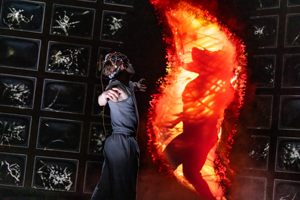 Louis McCartney as Henry Creel in Stranger Things: The First Shadow stands in front of a wall of screens that a creature cast in an orange glow has broken through. Louis McCartney as Henry Creel in Stranger Things: The First Shadow stands in front of a wall of screens that a creature cast in an orange glow has broken through.