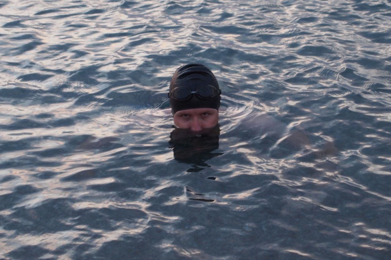 Immagine di un ragazzo dalla pelle chiara, con cuffia nera e occhialini che emerge dall'acqua del mare solo con la testa, fino all'altezza del naso. E guarda in camera con sguardo accigliato o minaccioso. Immagine di un ragazzo dalla pelle chiara, con cuffia nera e occhialini che emerge dall'acqua del mare solo con la testa, fino all'altezza del naso. E guarda in camera con sguardo accigliato o minaccioso.