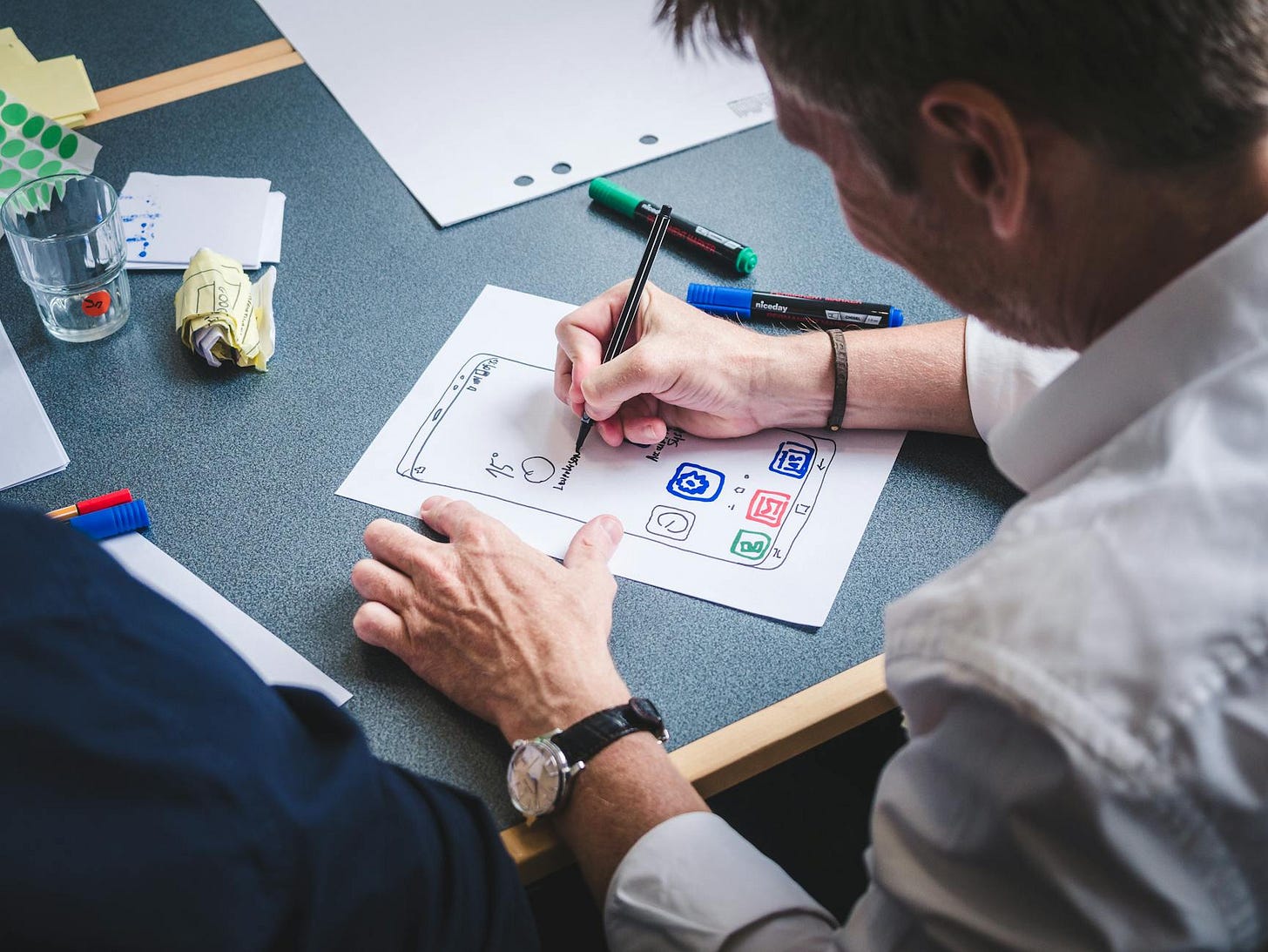 A designer sketches a mobile app prototype on paper at an office desk, focusing on creativity and design. A designer sketches a mobile app prototype on paper at an office desk, focusing on creativity and design.
