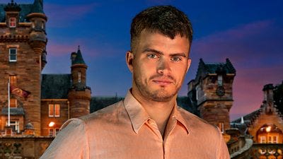 A man in a peach shirt smiles to camera, set against the backdrop of a castle by night A man in a peach shirt smiles to camera, set against the backdrop of a castle by night