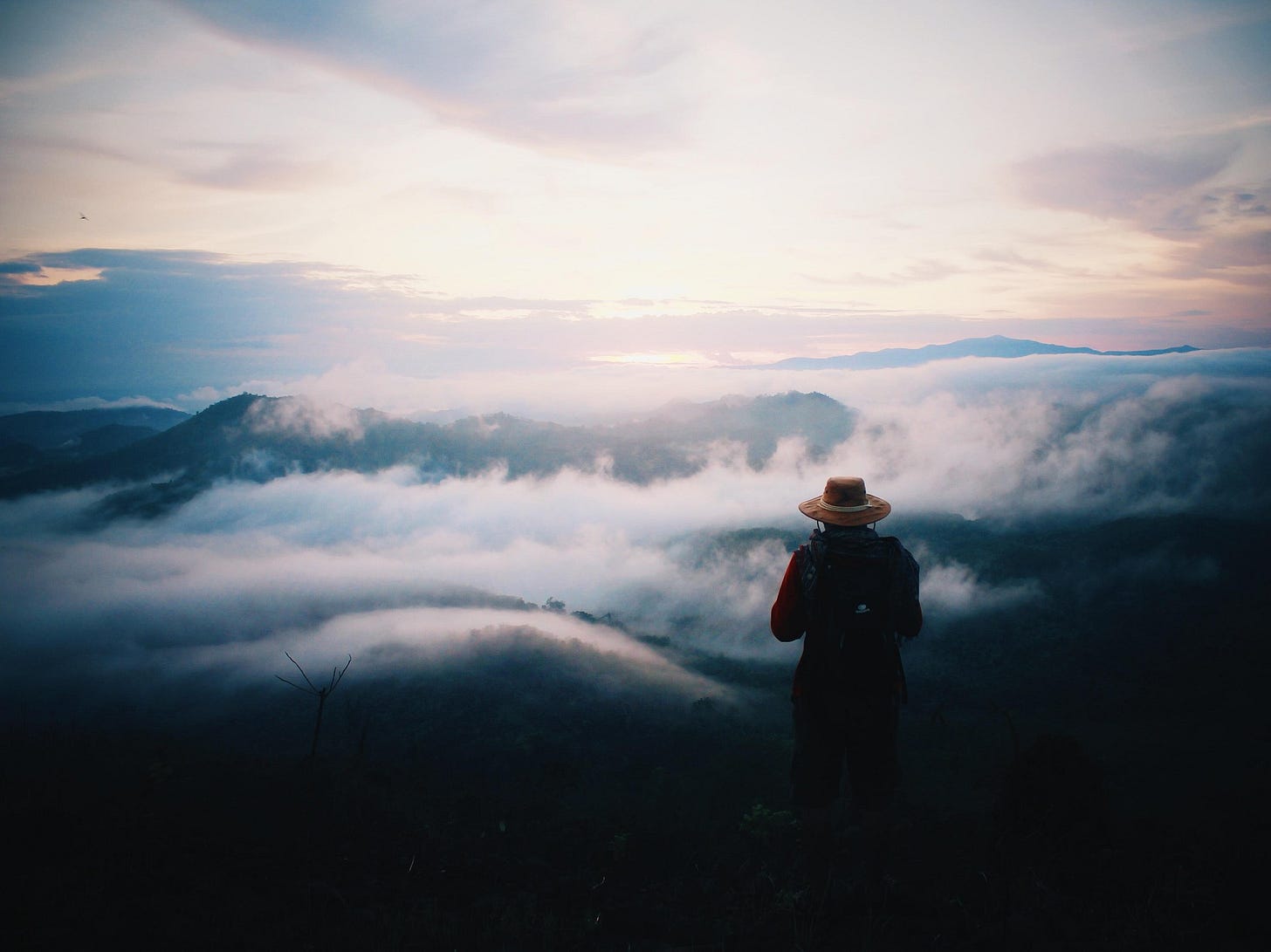 A man standing over fog-covered mountains with a sunrise in the distance.
