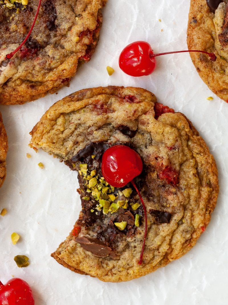 three spumoni cookies sit on a white background, with one cookie as the focal point. the central cookie has a bite taken out of it, and is topped with a red stemmed maraschino cherry