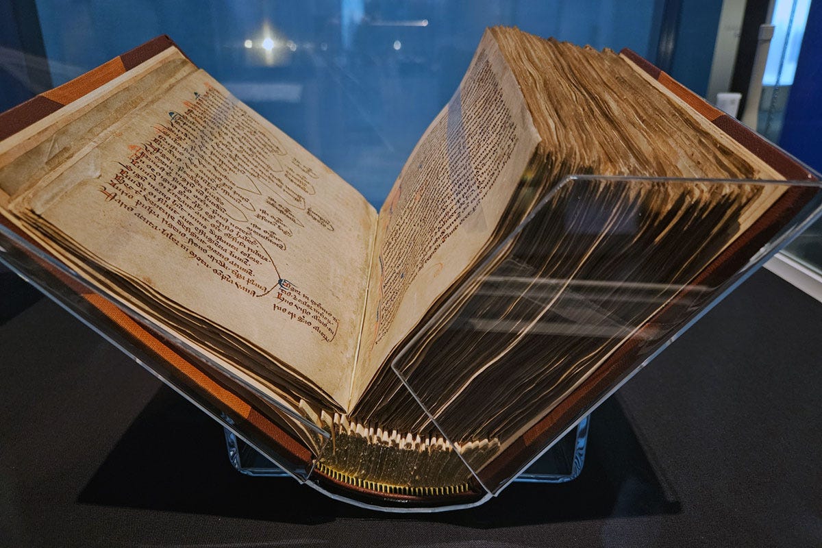A large medieval manuscript on display, propped open to show the inside pages