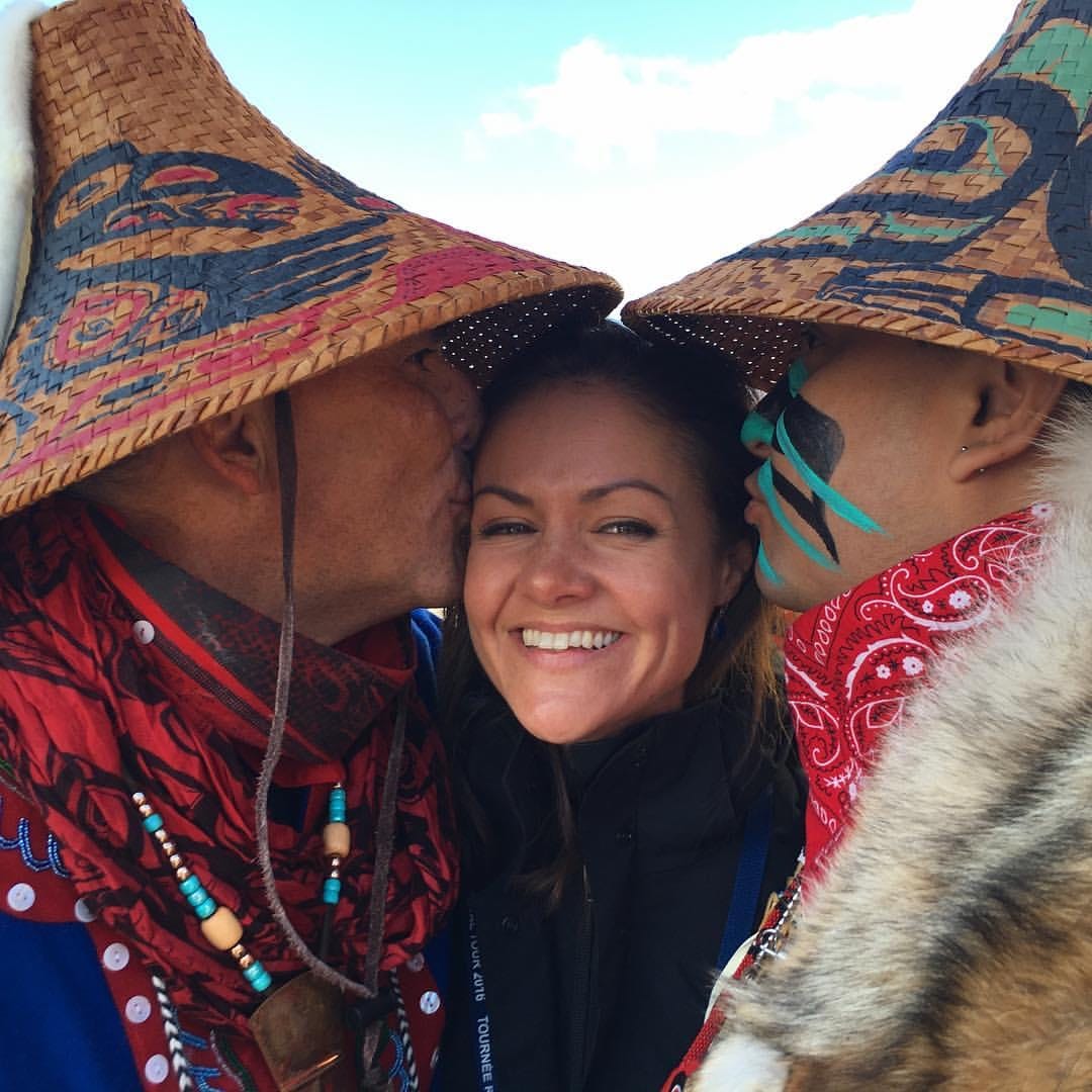 Emily Nash smiling being kissed on the cheeks by two men in native Canadian garb