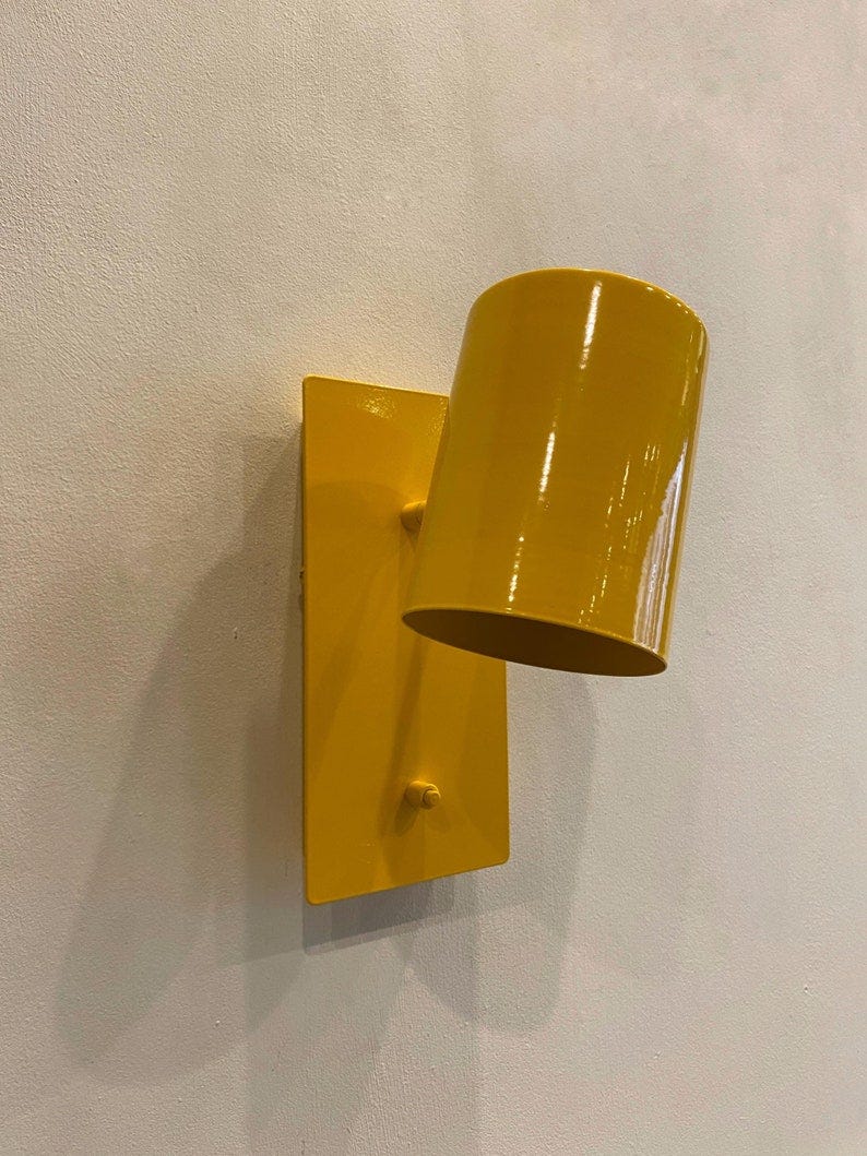 May include: A yellow wall-mounted light fixture with a cylindrical shade. The fixture is made of metal and has a simple, modern design. May include: A yellow wall-mounted light fixture with a cylindrical shade. The fixture is made of metal and has a simple, modern design.