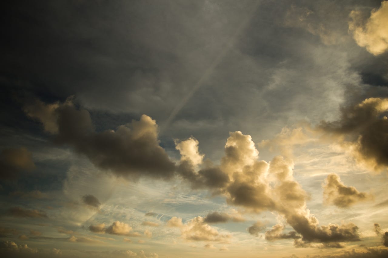 Dramatic sky with dark storm clouds and golden-lit cumulus clouds, with rays of light breaking through from the upper right.