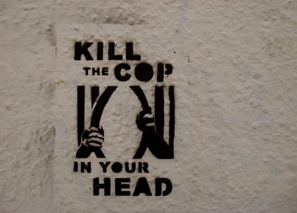 Graffiti that reads Kill the Cop in Your Head painted on a wall. Includes an image of someone bending jail cell bars open