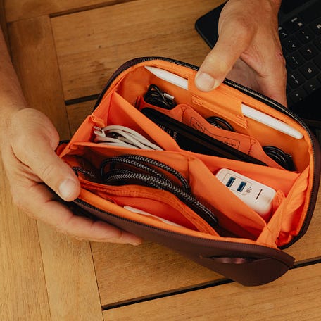 Person holding an Eclipse Tech Pouch Small with electronic accessories on a wooden surface