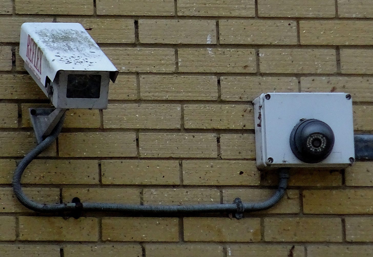 Two security cameras on a brick wall.