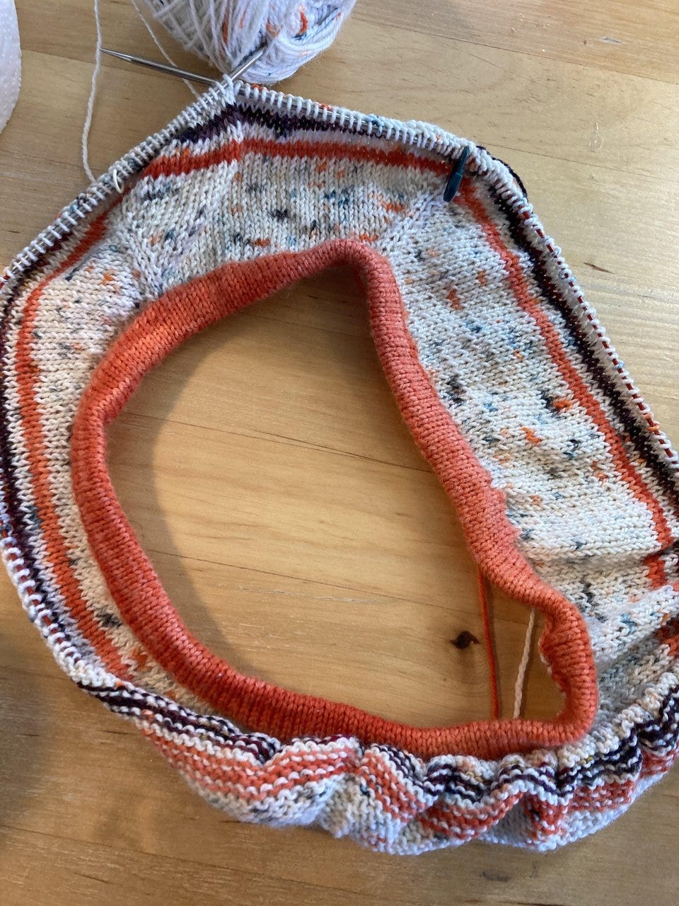 The yolk of a handknit raglan tee, knit in speckled white yarn with orange and dark purple stripes.