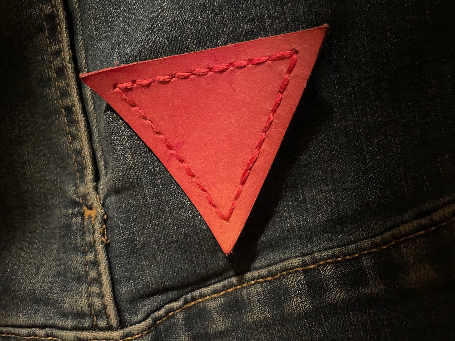 A leather pink triangle patch, sewn onto denim. A leather pink triangle patch, sewn onto denim.