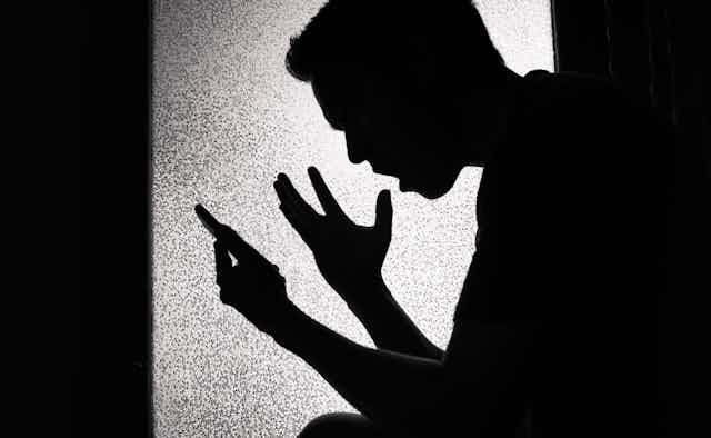Silhouette of upset young man looking at his smartphone screen. Silhouette of upset young man looking at his smartphone screen.