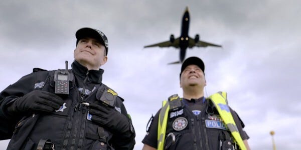 Two volunteer police officers at Stansted Airport with a large aircraft flying overhead