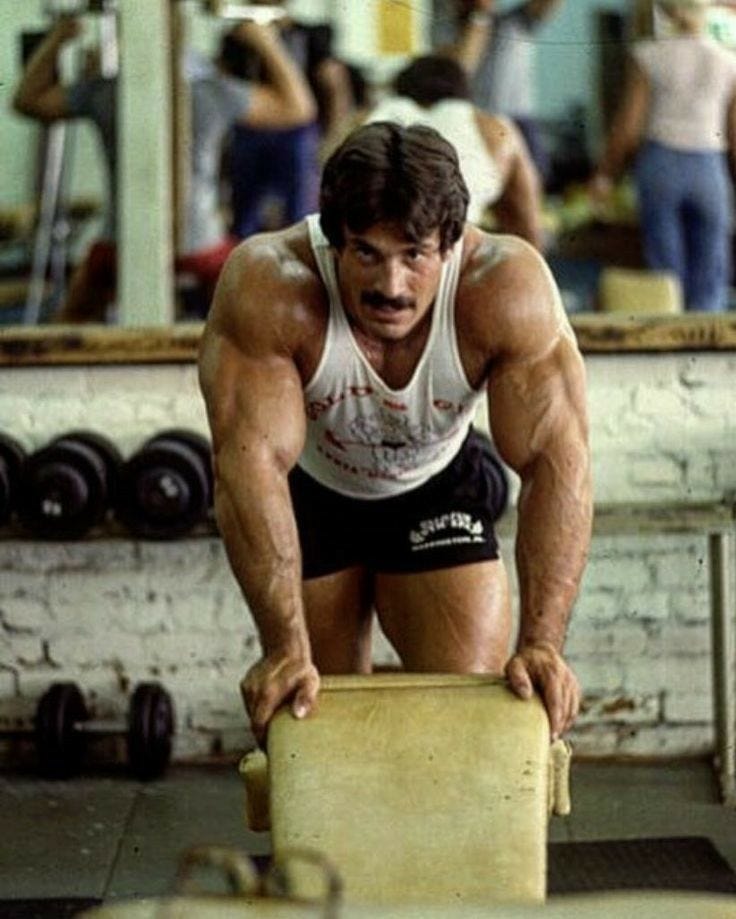 This may contain: a man squatting on a bench in a gym with other people working out behind him