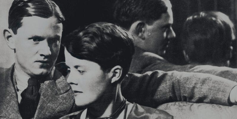 Black and white photo of a man in a suit with his arm around a young woman with short hair.