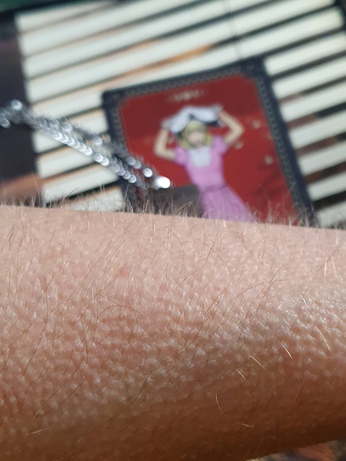 Close-up of goosebumps on a person's forearm, with a silver necklace chain and a blurred Fool tarot card showing a blonde figure in a pink dress against a red background. Close-up of goosebumps on a person's forearm, with a silver necklace chain and a blurred Fool tarot card showing a blonde figure in a pink dress against a red background.