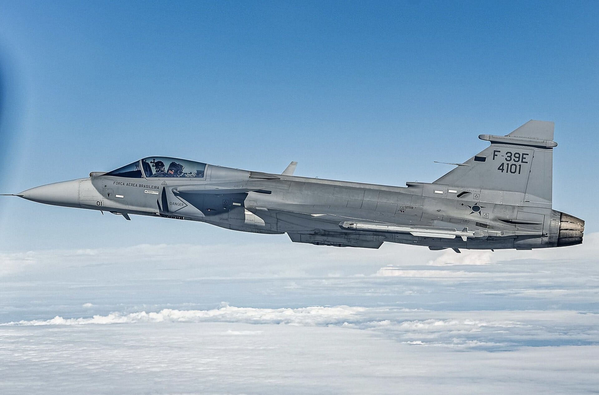 A grey Brazilian Air Force F-39E Gripen fighter with tail number 4101 flying above a layer of white clouds.