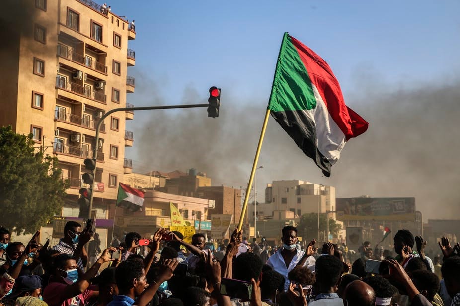 Hundreds of youthful protesters carry the Sudanese flag on sticks. Hundreds of youthful protesters carry the Sudanese flag on sticks.