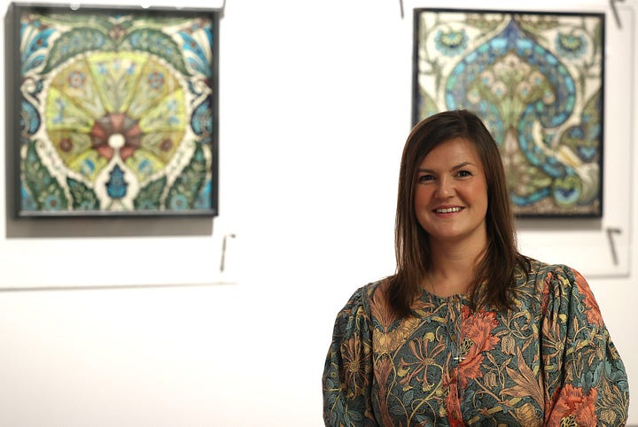 Image of a dark haired lady standing in front of pictures on a white wall. An old chrrch 