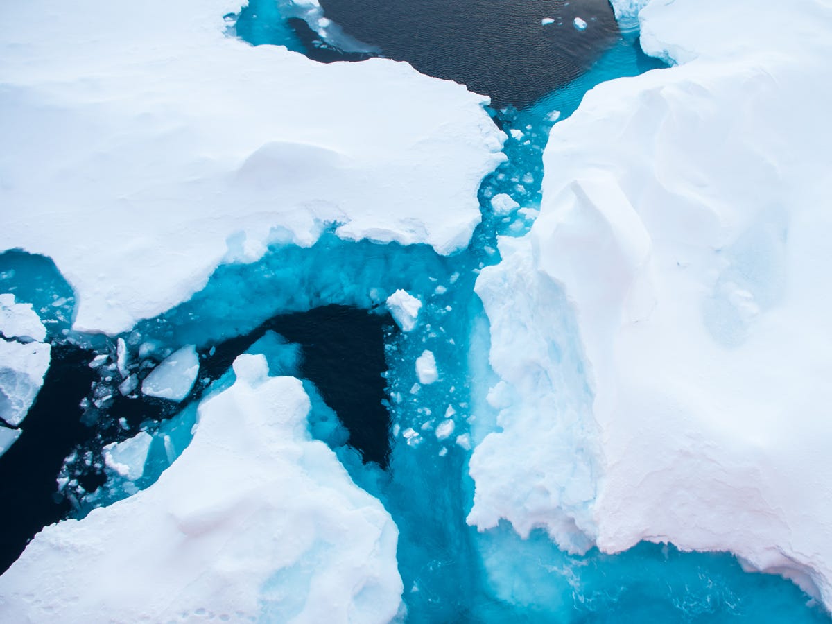 White floating sea ice has jagged edges where it meets the dark and light blue ocean waters. White floating sea ice has jagged edges where it meets the dark and light blue ocean waters.
