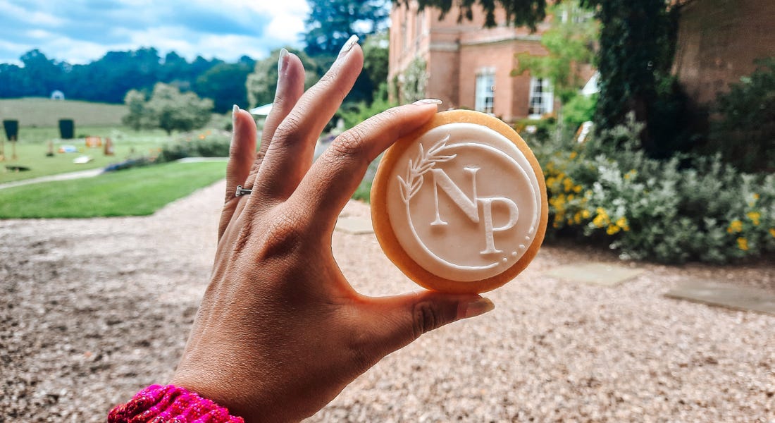 A hand holding a biscuit that says 'NP' with a building and lawn in the background A hand holding a biscuit that says 'NP' with a building and lawn in the background