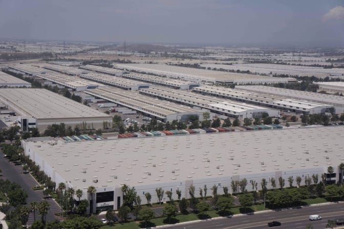 An aerial view of the roofs of vast grey warehouses, stretching far into the horizon