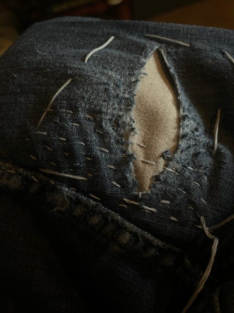 A piece of jean fabric is being repaired with visible stitches