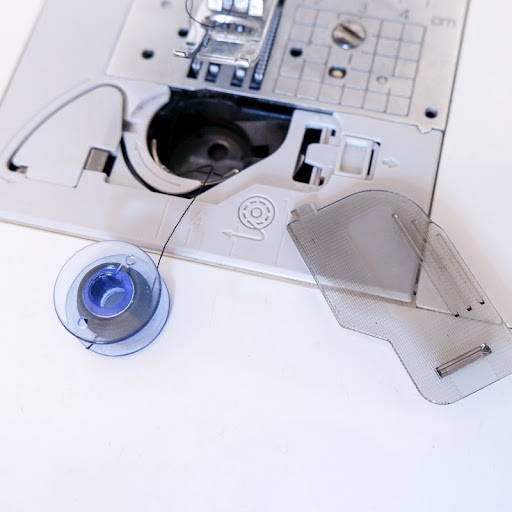 a bobbin with thread next to the bobbin compartment on a top loading sewing machine