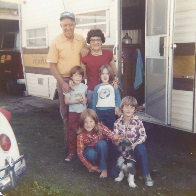 Four kids, a dog and their grandparents posing in front of a 1970s RV.