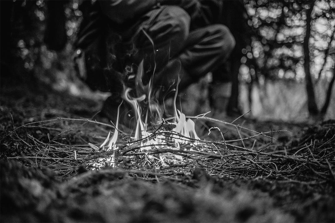 Person kneeling to watch a twig fire Person kneeling to watch a twig fire