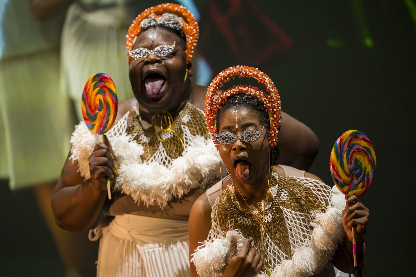 Two cheerful performers with colorful lollipops and sparkly accessories pose on stage. Two cheerful performers with colorful lollipops and sparkly accessories pose on stage.