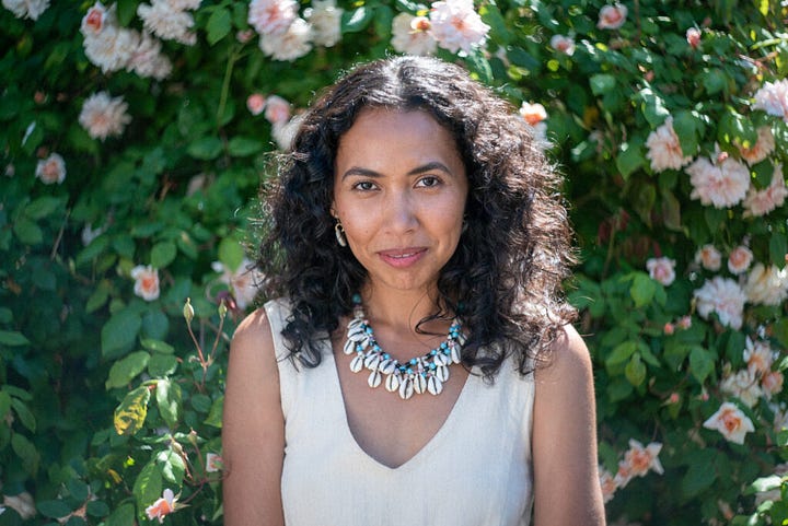 Two portraits of woman. Kailea is wearing a cowry shell necklace, standing in front of a rose bush. Kate is looking over her shoulder to a point to the left of the camera, wearing a red blouse. 