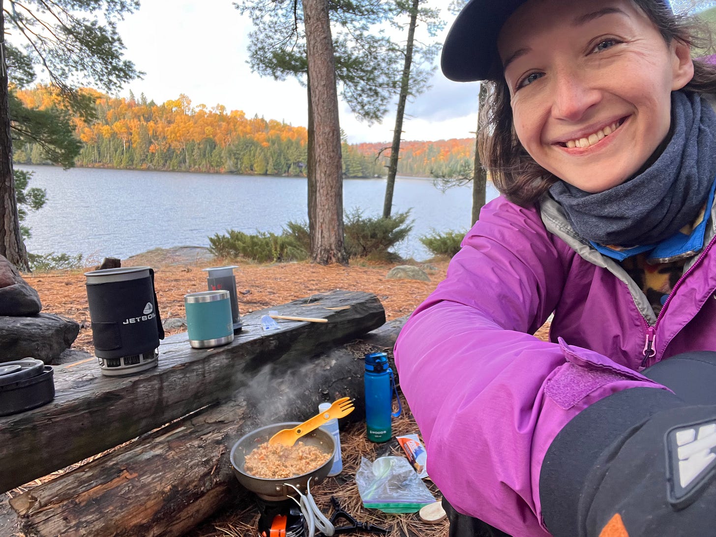 my campsite in the morning, in front of my a jetboil camping stove and yeti coffe cup raise on a long, steam rises from a pan of rice that is cooking on the ground, a spork sticking out of the messy pile of mush, camping gear is scattered everywhere