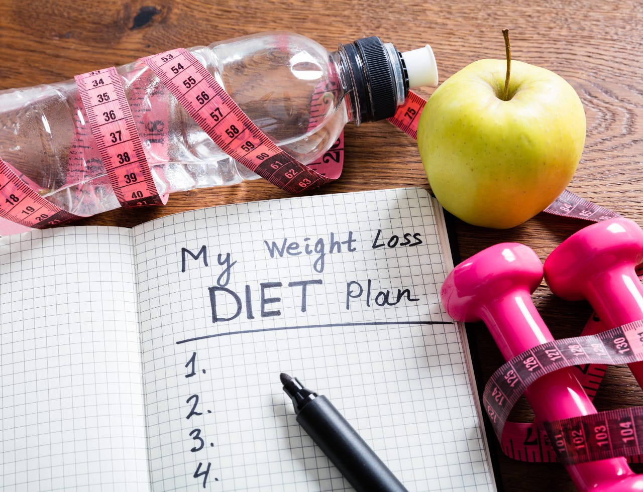 pen book measuring tape water bottle and dumbbells creating a weight loss diet plan